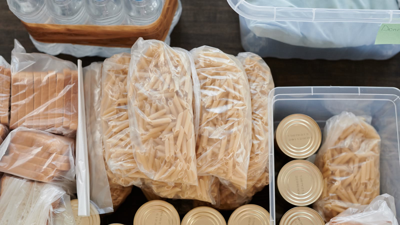 Plastkasse med konservesdåser og pasta set fra oven ved siden af vand og brød